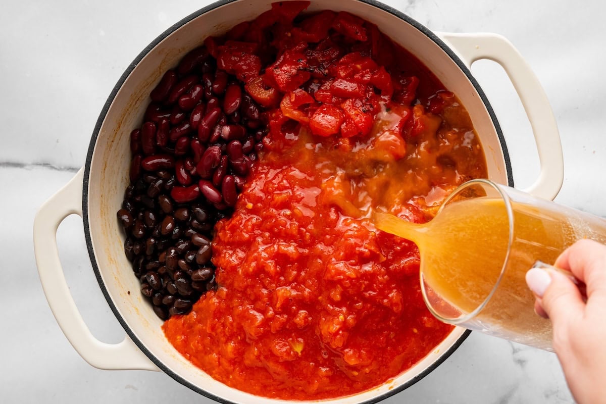 Broth, pumpkin purée, beans and tomatoes added to browned meat in a Dutch oven.
