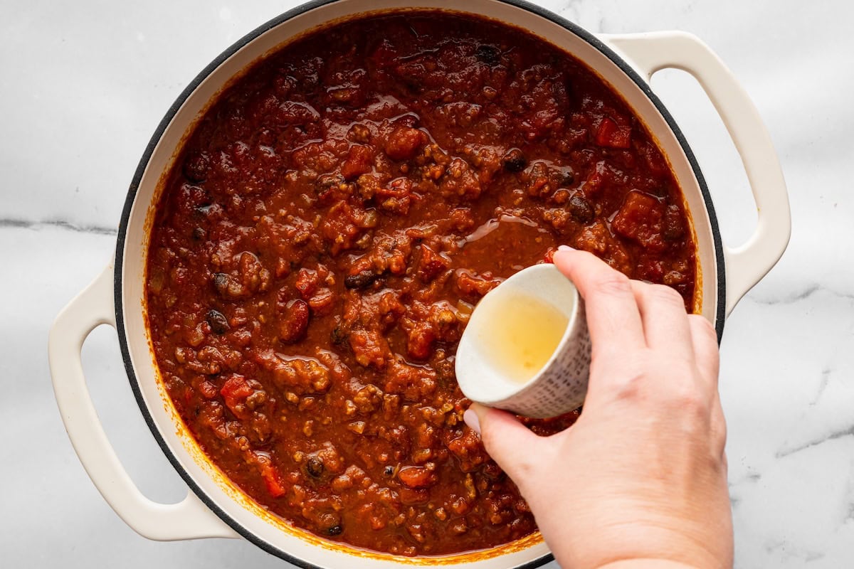 Apple cider vinegar being added to a pot of finished pumpkin chili.
