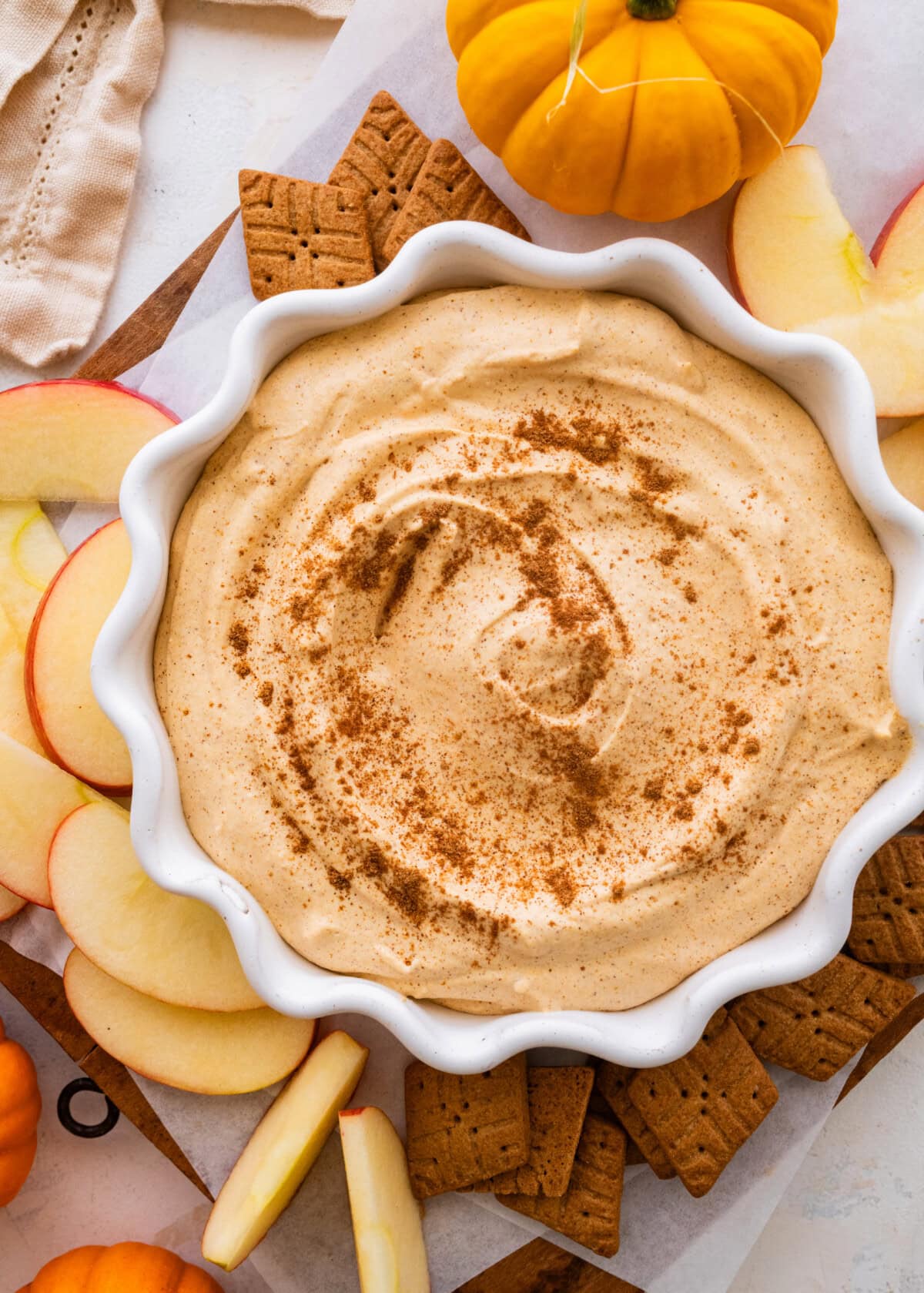 A bowl with pumpkin fluff dip with crackers and apple slices to the side.