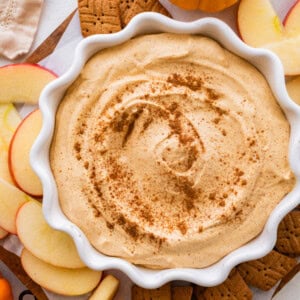 A bowl with pumpkin fluff dip with crackers and apple slices to the side.