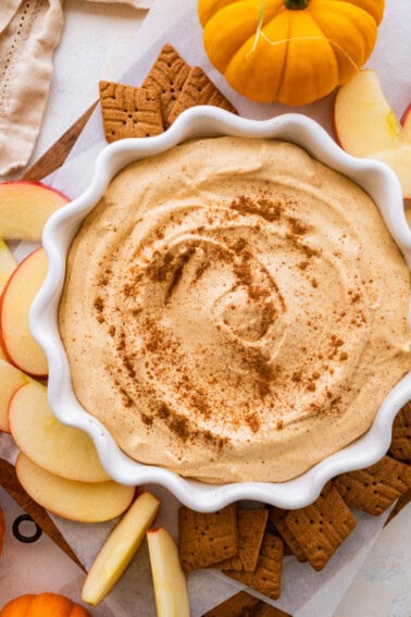 A bowl with pumpkin fluff dip with crackers and apple slices to the side.