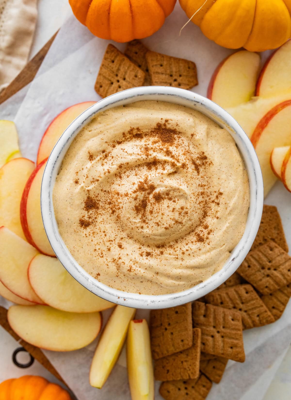 Pumpkin fluff dip in a small bowl on a plate with sliced apples and crackers.