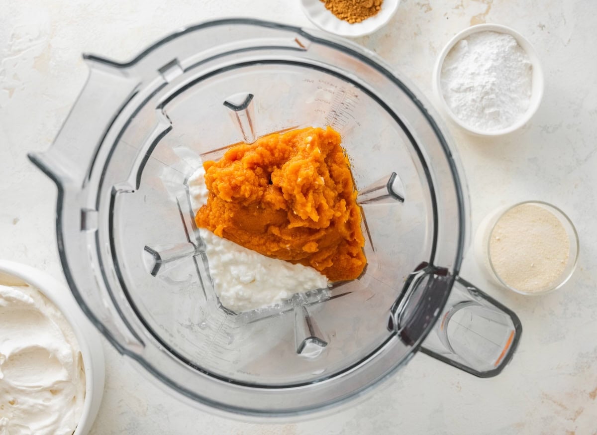 A blender with ingredients used for pumpkin fluff dip.