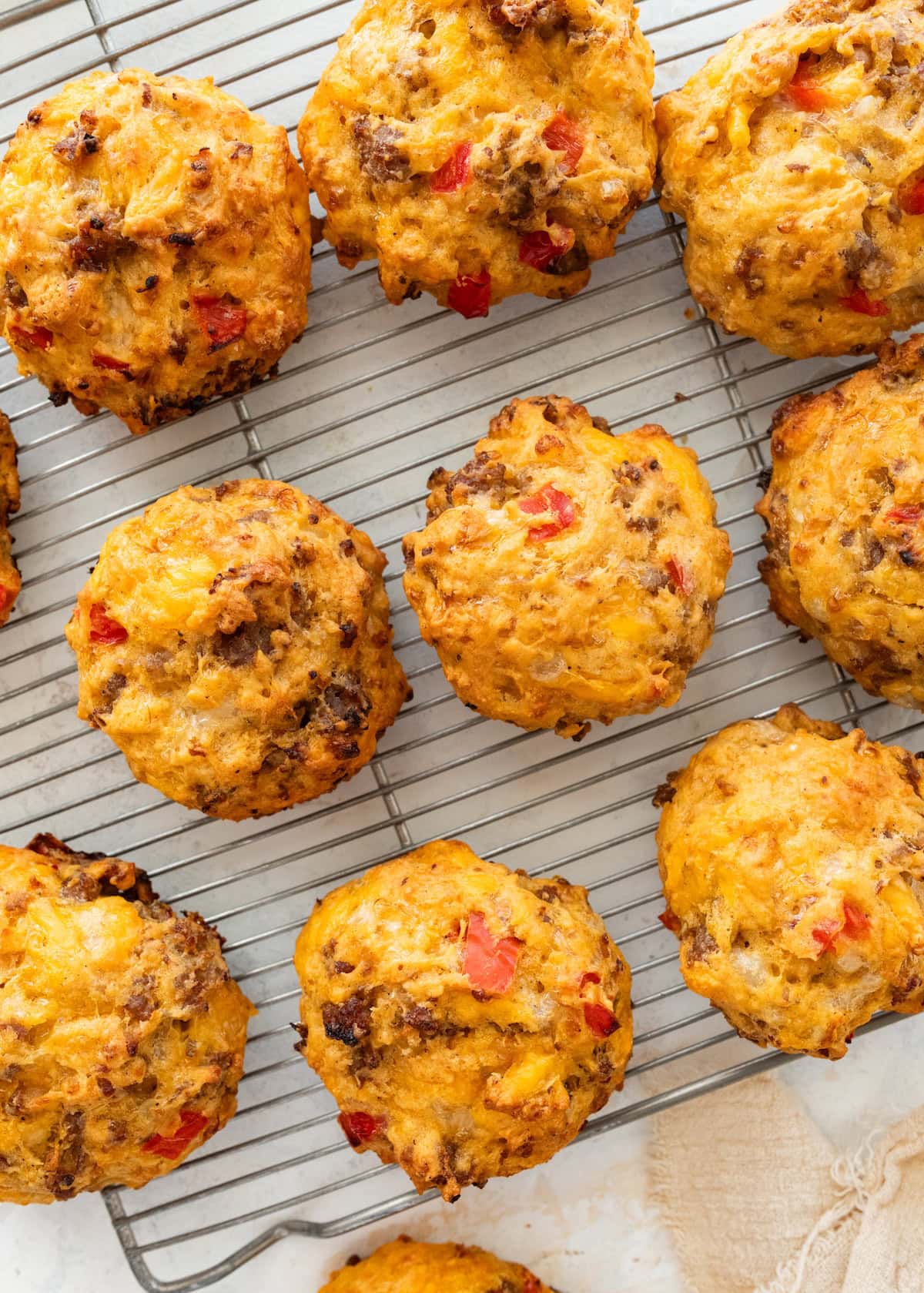 Overhead view of golden breakfast biscuits with sausage, red bell pepper and cheddar on a cooling rack.