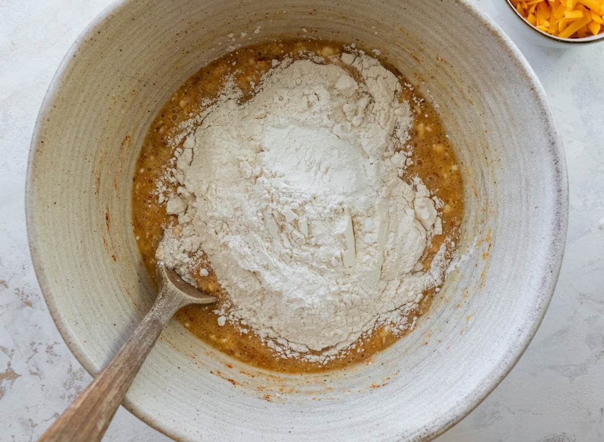Flour and baking powder added to the wet ingredients in a mixing bowl.