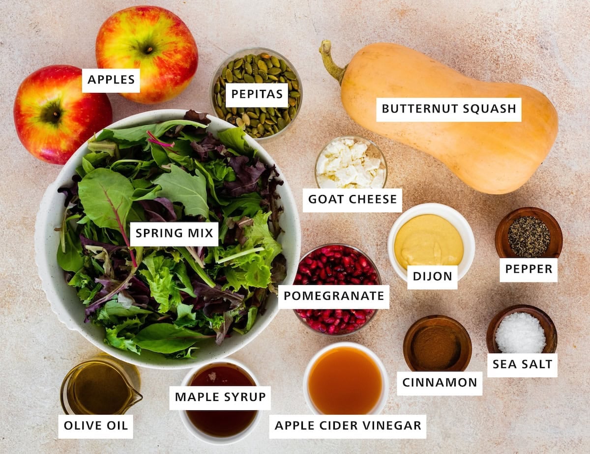 Ingredients measured out to make Thanksgiving Salad: olive oil, spring mix, apples, maple syrup, pepitas, pomegranate, goat cheese, vinegar, cinnamon, dijon, butternut squash, sea salt and pepper.