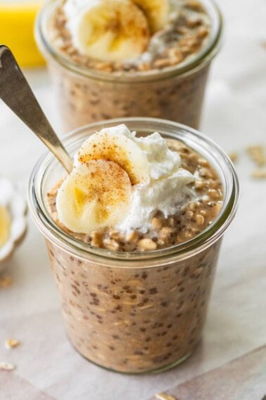 Two glass jars with banana bread latte overnight oats topped with greek yogurt and banana slices.