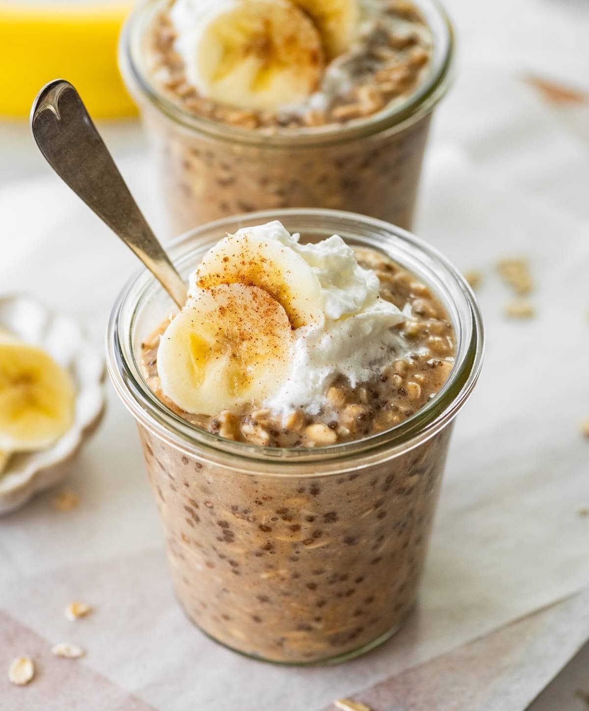 Two glass jars with banana bread latte overnight oats topped with greek yogurt and banana slices.
