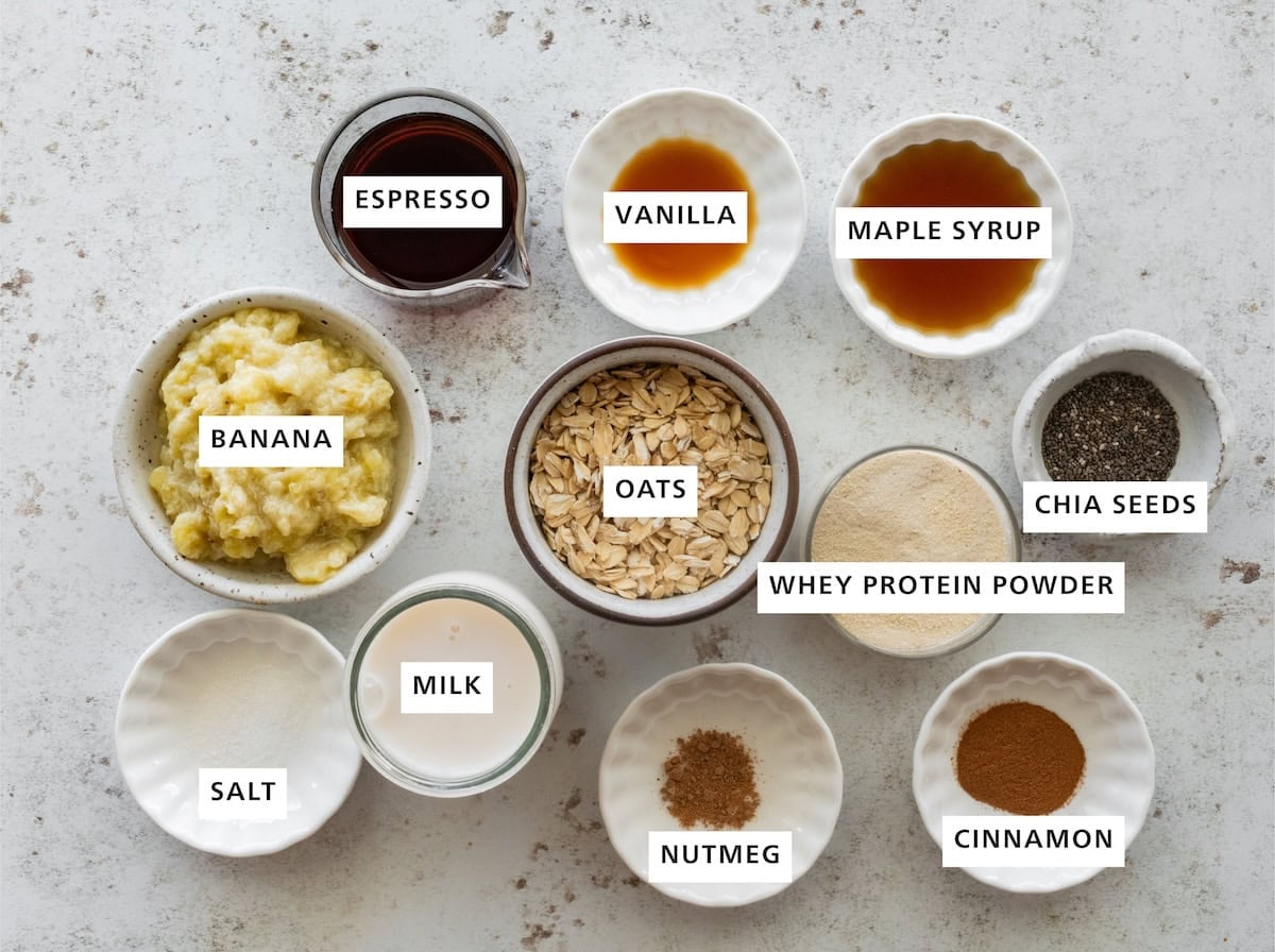 Ingredients measured out for banana bread latte overnight oats include: oats, whey protein powder, cinnamon, nutmeg, milk, salt, banana, espresso, vanilla, maple syrup, and chia seeds.