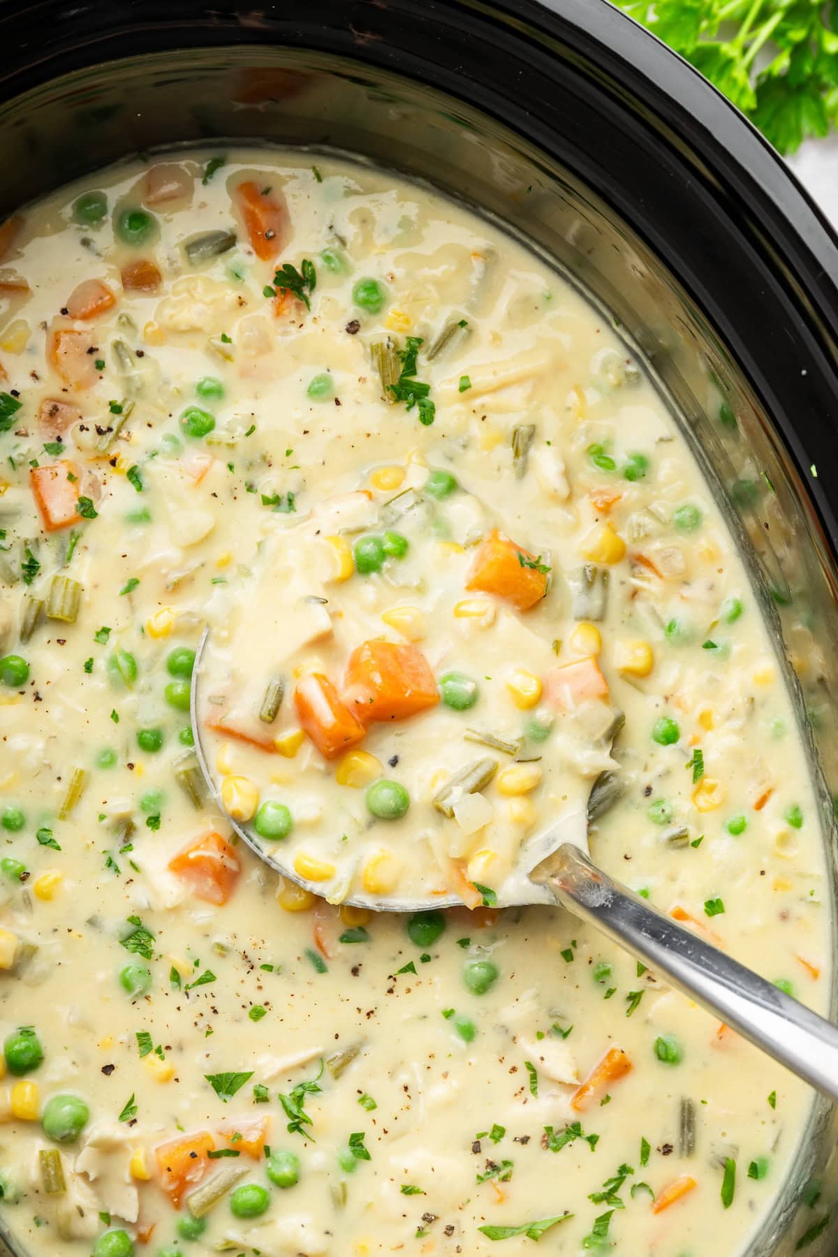 Angled view of chicken pot pie soup in a slow cooker with a ladle resting in the creamy broth.