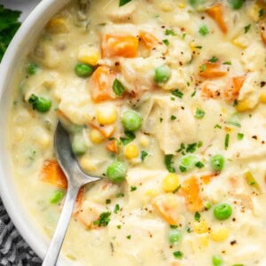 Close-up of creamy chicken pot pie soup with chunks of chicken, carrots, peas, corn and parsley.