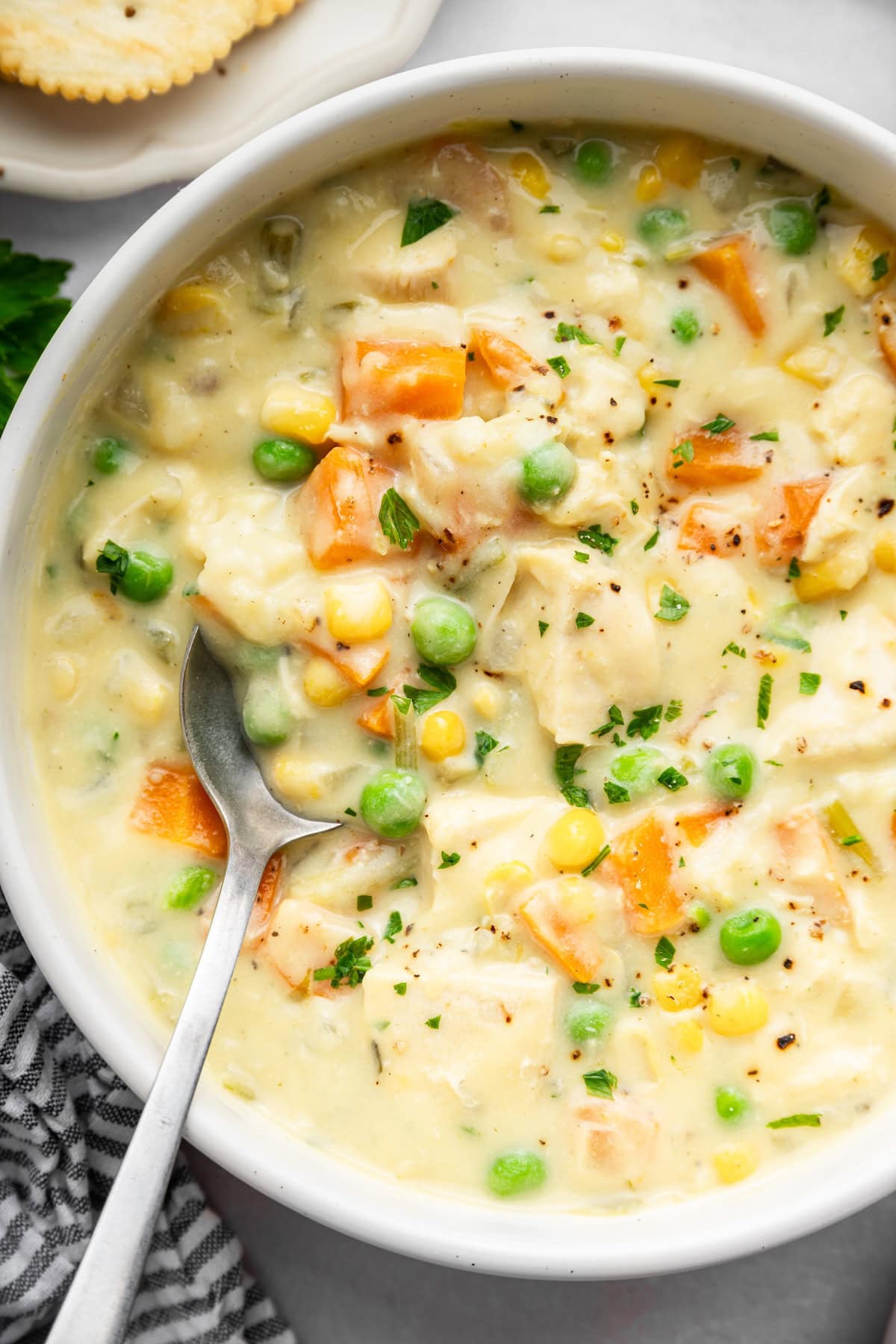 Close-up of creamy chicken pot pie soup with chunks of chicken, carrots, peas, corn and parsley.