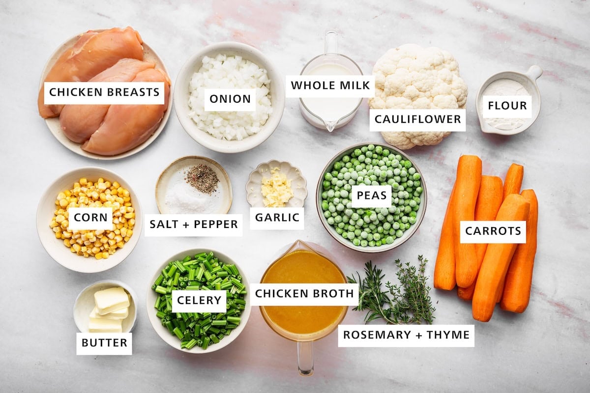 Ingredients measured out for chicken pot pie soup includes: chicken breasts, onion, whole milk, cauliflower, flour, carrots, rosemary, thyme, chicken broth, celery, butter, corn, salt, pepper, garlic, and peas.