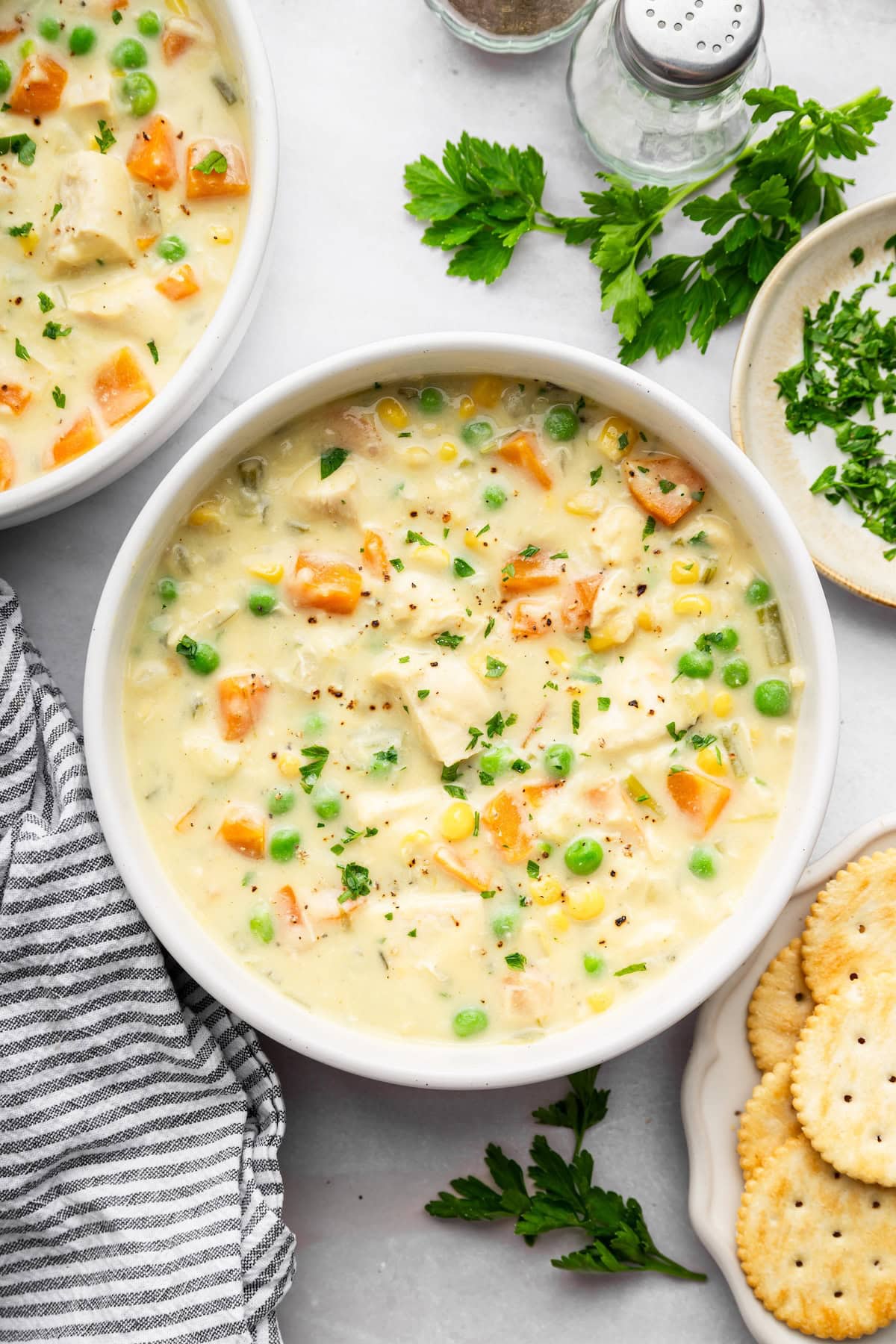 Overhead view of chicken pot pie soup in a white bowl topped with chopped parsley.
