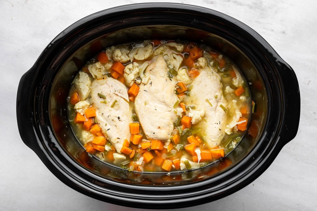 Cooked chicken, cauliflower, carrots and celery in broth in a slow cooker.