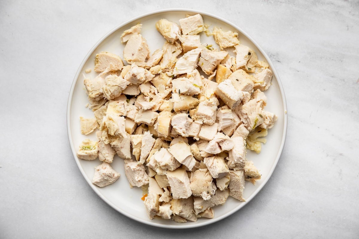 Cooked chicken breasts chopped into bite-size pieces on a white plate.