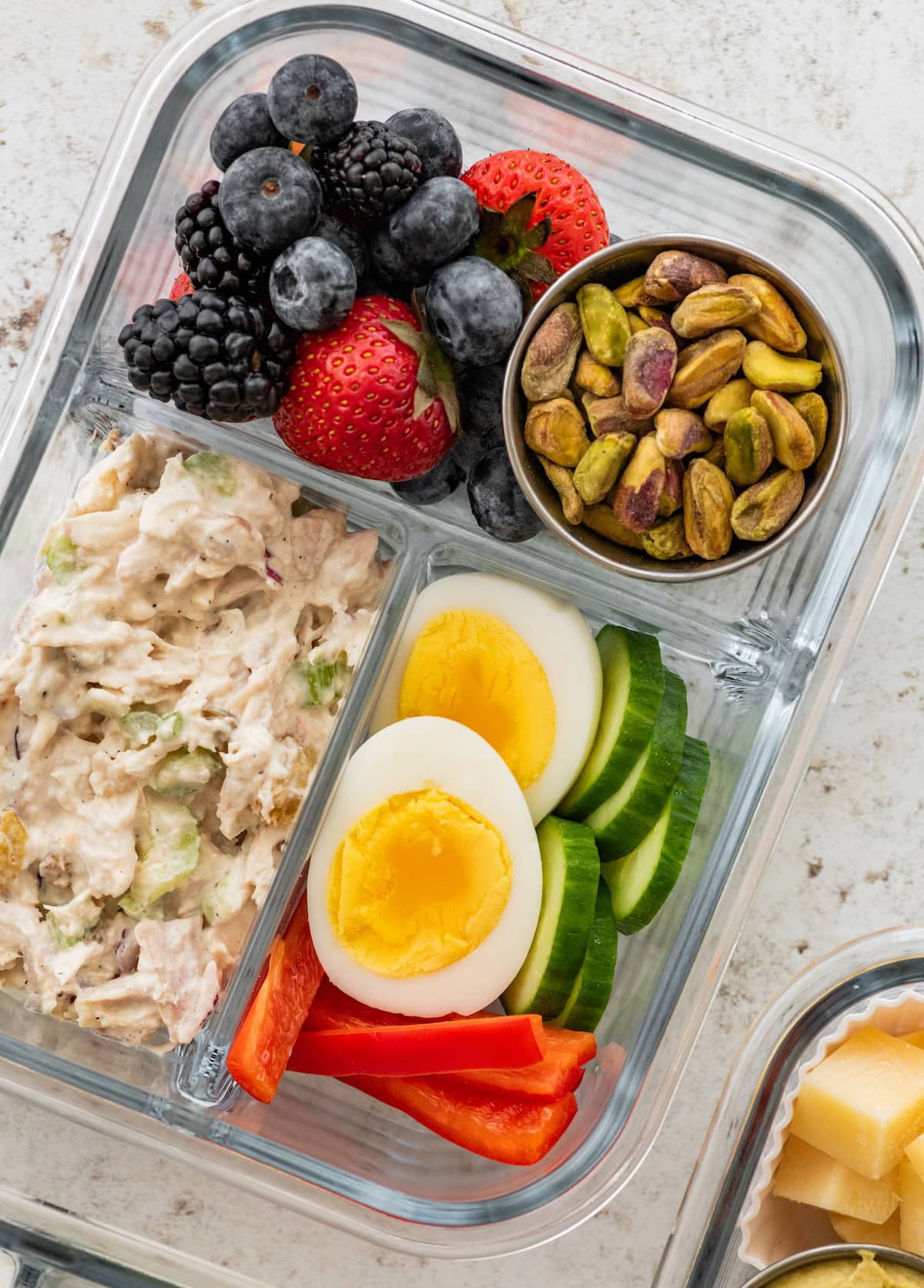 Chicken salad protein box with a hard-boiled egg, cucumber, red bell pepper, pistachios and mixed berries.