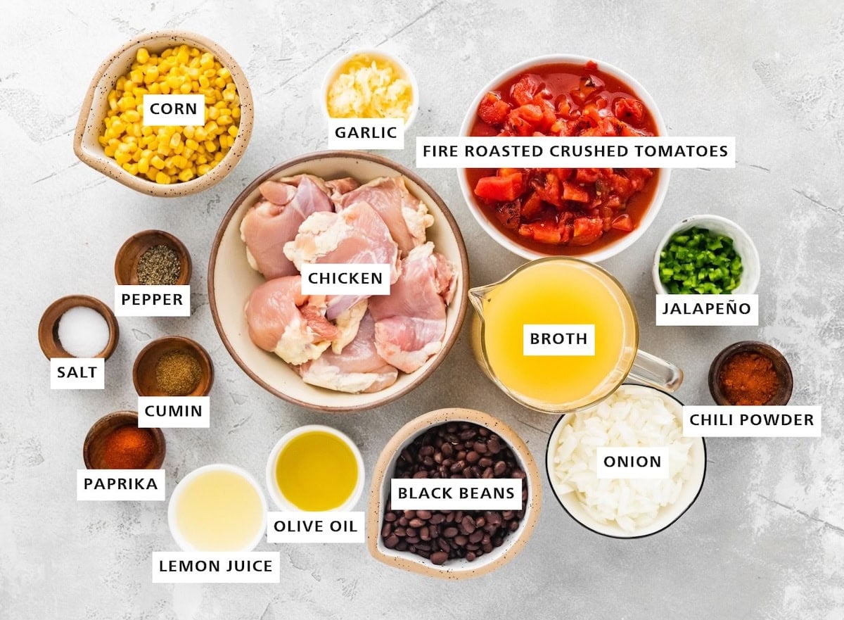 Ingredients measured out to make Chicken Tortilla Soup: chili powder, jalapeño, onion, broth, fire roasted crushed tomatoes, black beans, garlic, chicken, olive oil, lime juice, corn, pepper, cumin, paprika and sea salt.