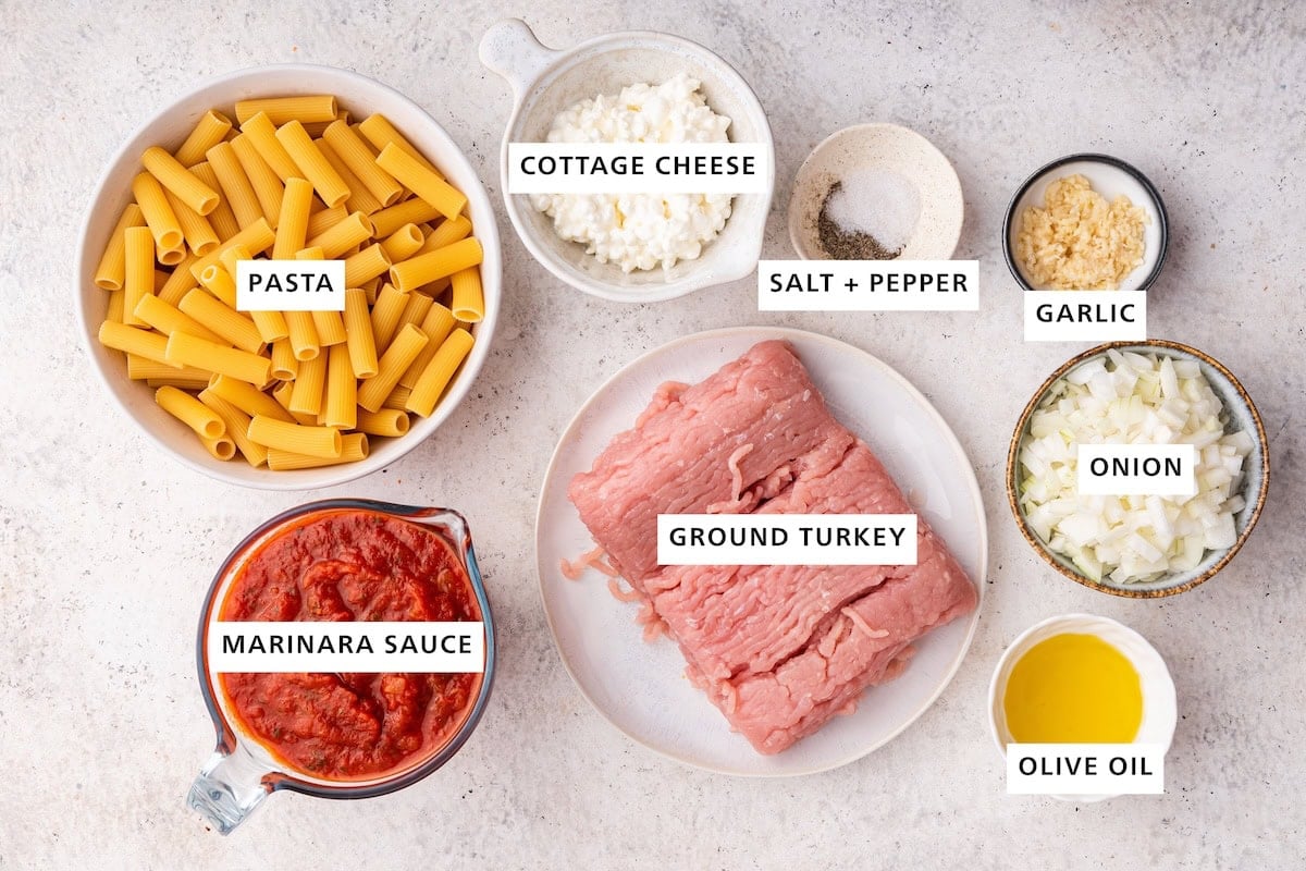Ingredients measured out to make Creamy Cottage Cheese Pasta: marinara sauce, pasta, ground turkey, cottage cheese, salt, pepper, olive oil, yellow onion and garlic.