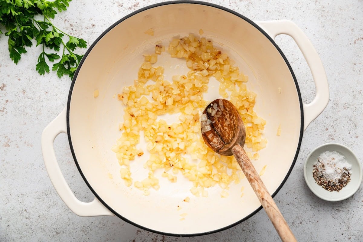 Diced onion and minced garlic sautéing in a Dutch oven with a wooden spoon.