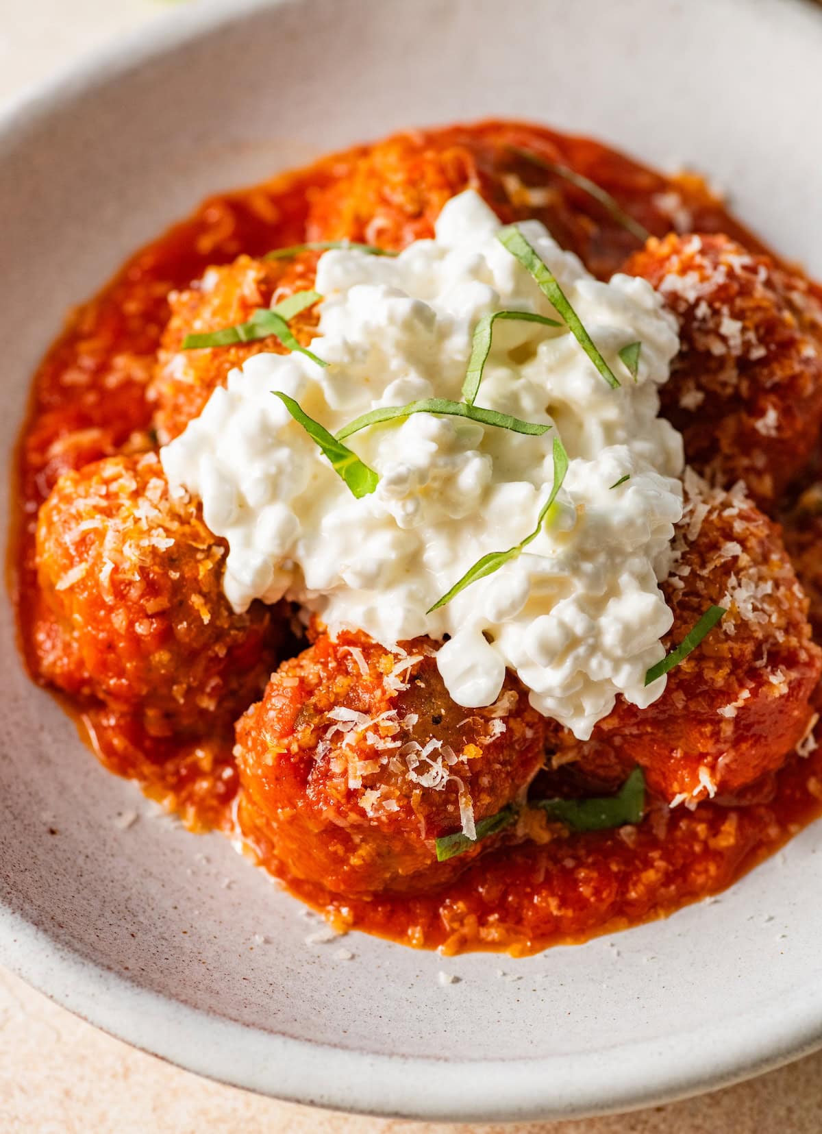 Close-up of chicken meatballs in marinara topped with a generous scoop of cottage cheese, Parmesan and sliced basil.