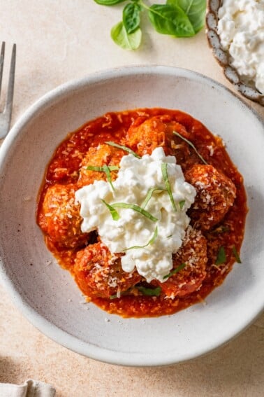 Overhead view of Hailey Bieber meatballs with marinara, cottage cheese, Parmesan and basil in a bowl.