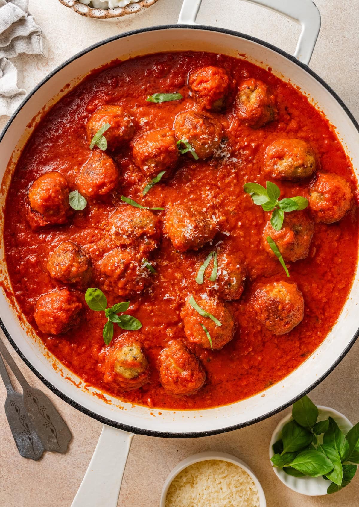 Overhead view of chicken meatballs simmering in marinara sauce with fresh basil in a skillet.