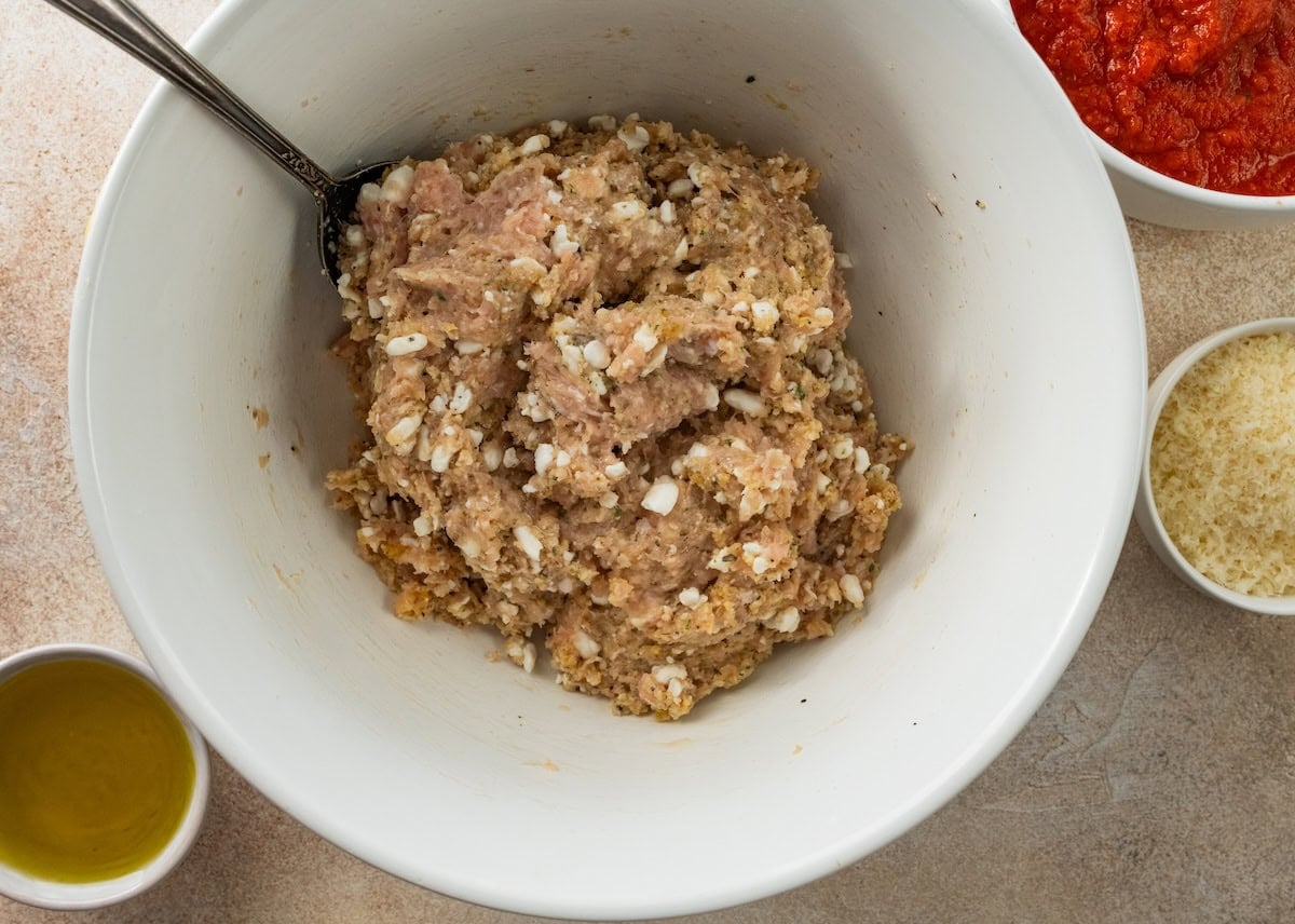 Ground chicken meatball mixture with cottage cheese, breadcrumbs and seasonings in a mixing bowl.