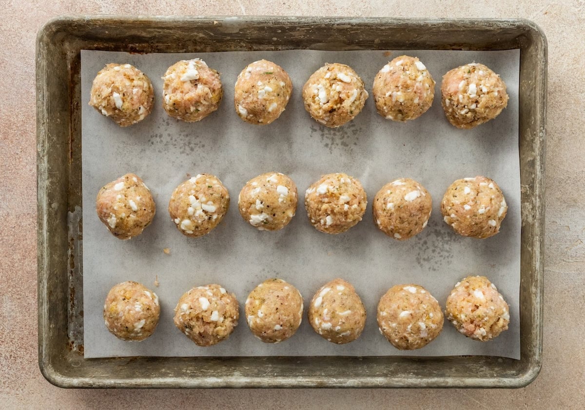 Uncooked chicken and cottage cheese meatballs arranged on a parchment-lined baking sheet.
