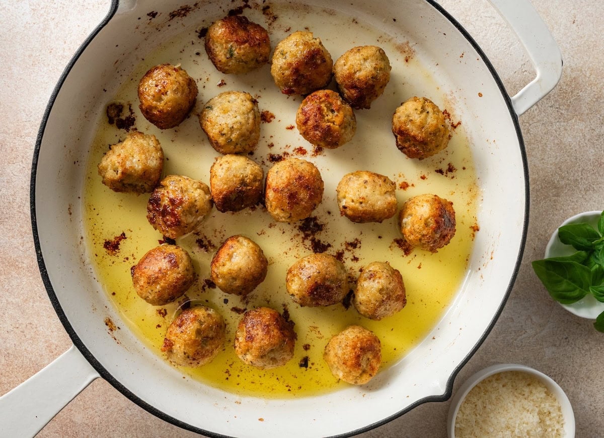 Chicken meatballs browned on several sides in a skillet with olive oil.
