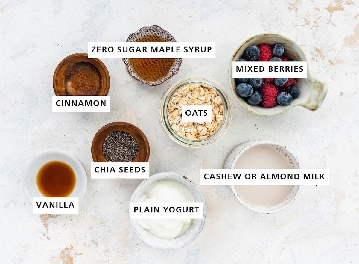 Ingredients measured out to make Low Calorie Overnight Oats: mixed berries, cashew or almond milk, oats, maple syrup, plain yogurt, chia seeds, cinnamon and vanilla.