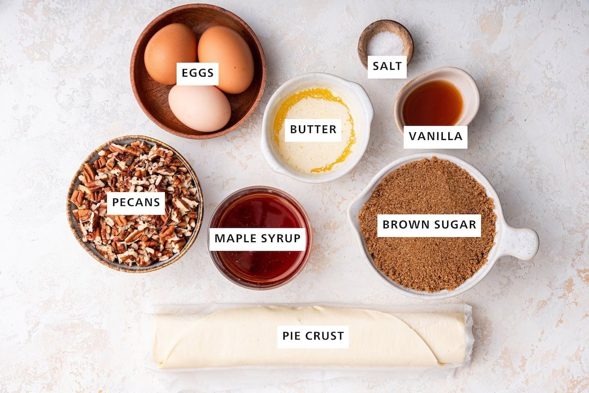 Ingredients measured out to make Easy Pecan Pie: pie crust, pecans, maple syrup, eggs, butter, brown sugar, vanilla and salt.
