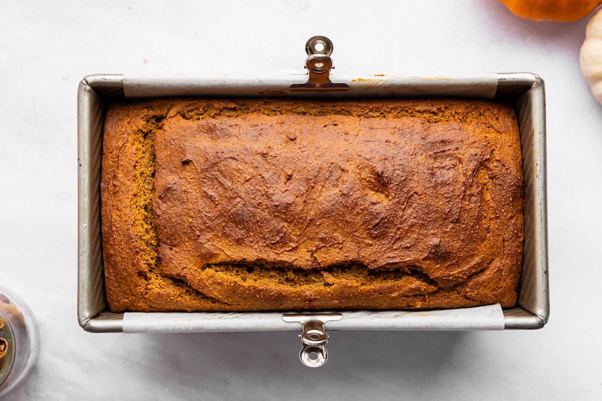 Baked pumpkin bread with a golden brown top in a parchment-lined loaf pan.