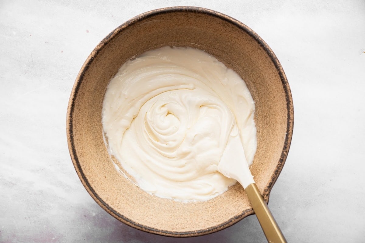 Creamy cottage cheese frosting in a bowl with a spatula.