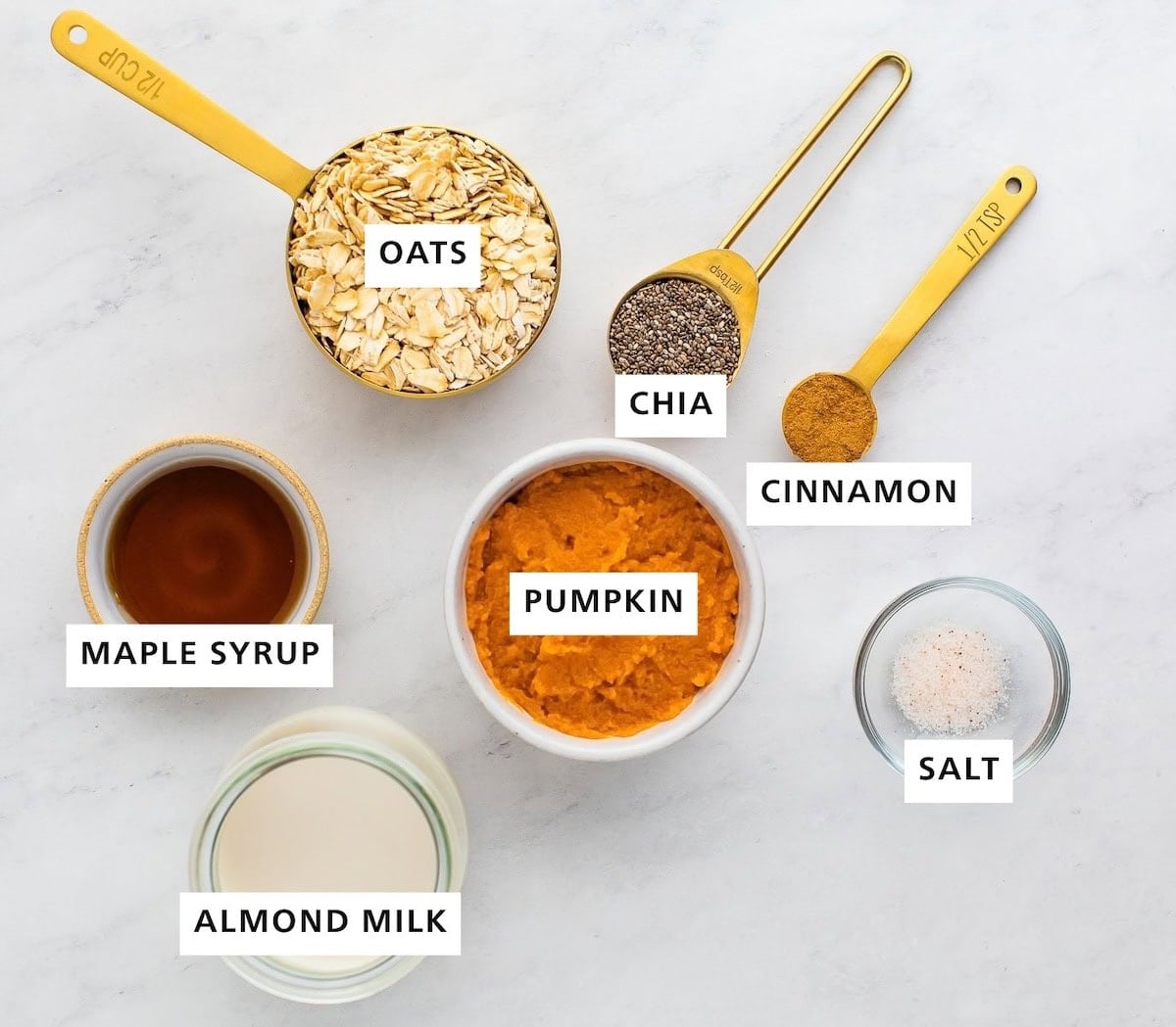 Ingredients measured out to make pumpkin overnight oats: maple syrup, almond milk, oats, pumpkin, chia seeds, cinnamon and salt.