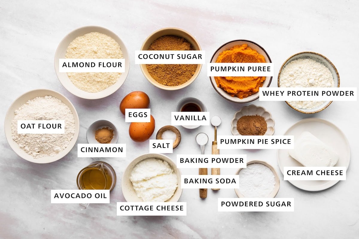 Ingredients measured out for pumpkin protein bread include: pumpkin puree, whey protein powder, pumpkin pie spice, cream cheese, powdered sugar, baking powder, baking soda, vanilla, salt, eggs, cinnamon, avocado oil, cottage cheese, oat flour, almond flour, and coconut sugar.