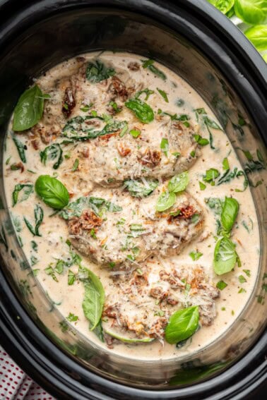 Overhead view of slow cooker marry me chicken topped with Parmesan and fresh basil.