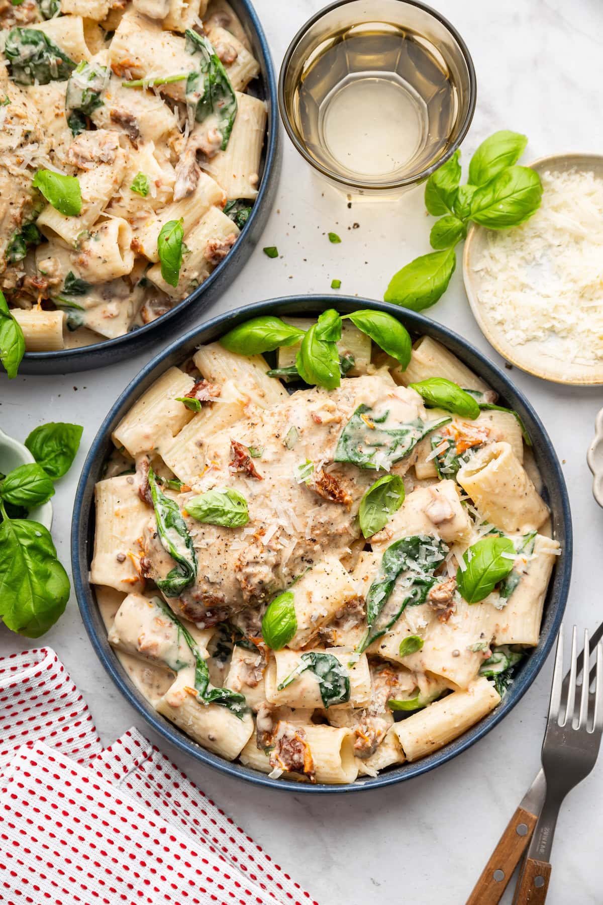 Slow cooker marry me chicken served over pasta in bowls with fresh basil and grated Parmesan.