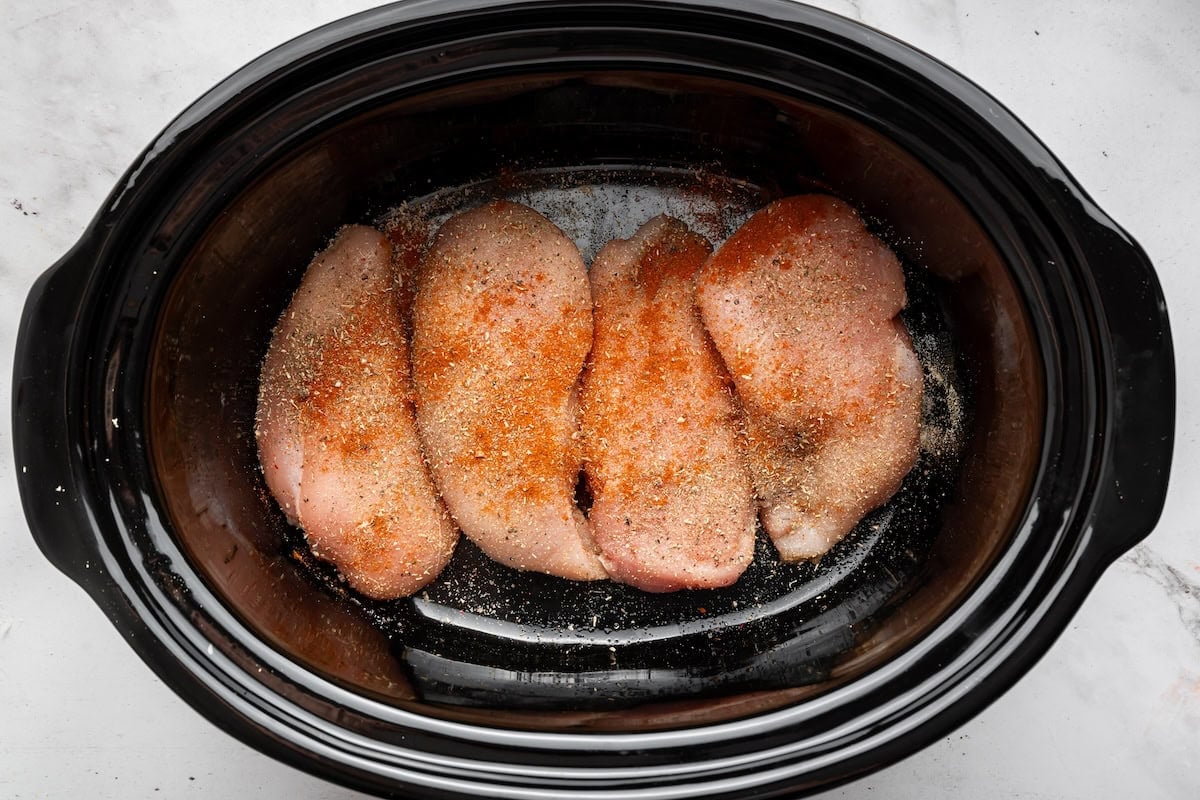 Raw chicken breasts sprinkled with seasonings in the slow cooker.