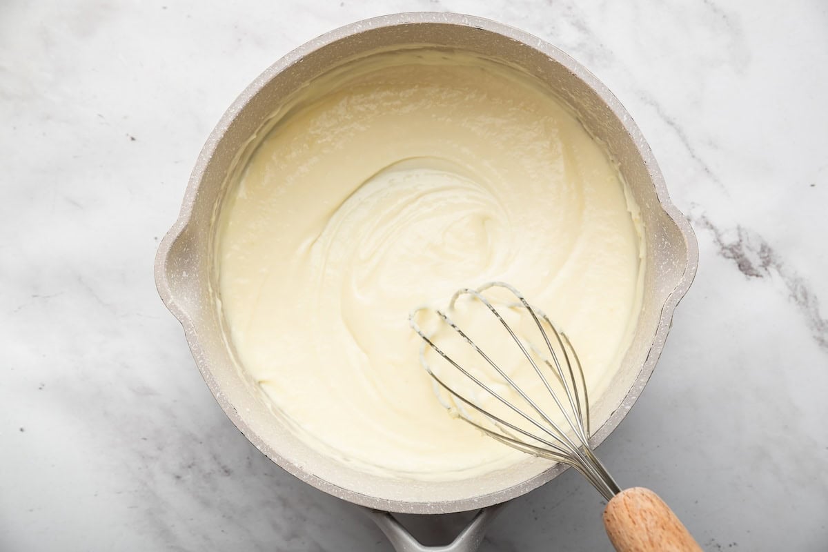Creamy Parmesan sauce in a saucepan with a whisk.