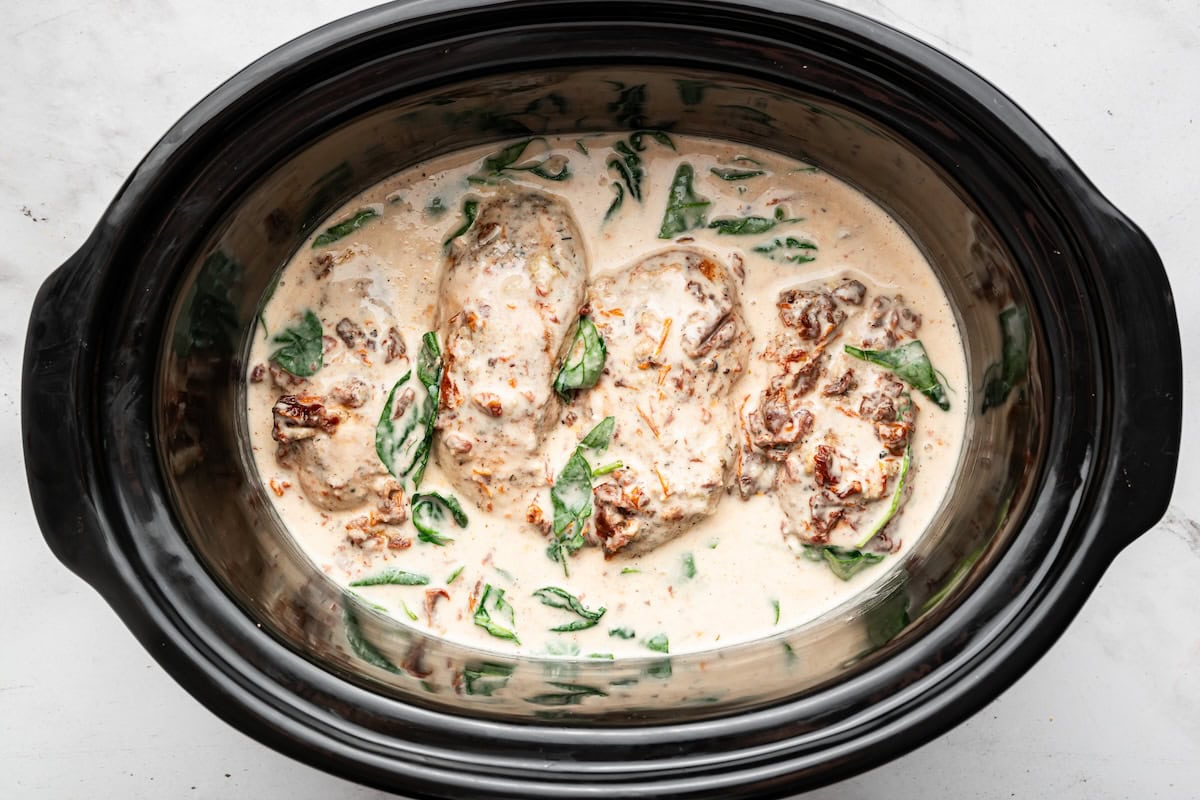 Cooked chicken breasts in a slow cooker with creamy Parmesan sauce, spinach and sun-dried tomatoes.