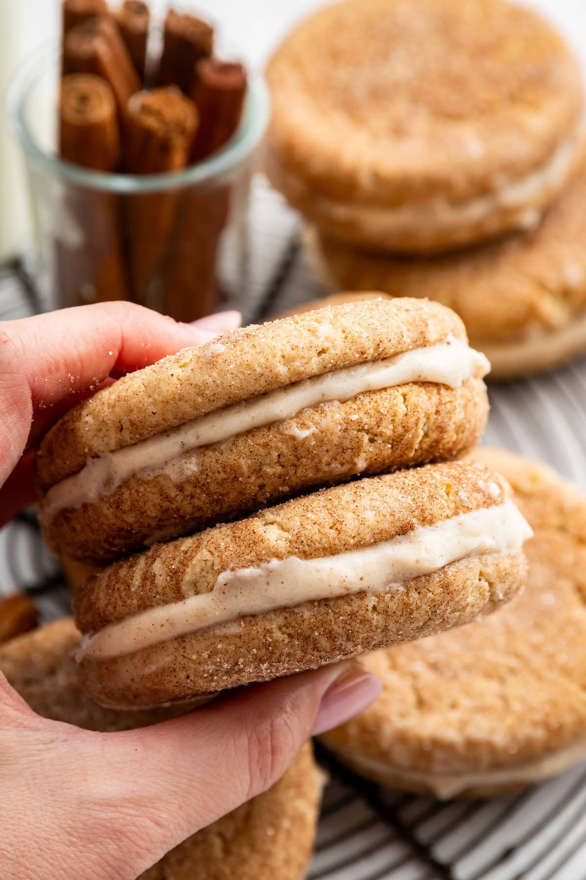 Hand holding a snickerdoodle sandwich cookie with cinnamon cream cheese frosting.