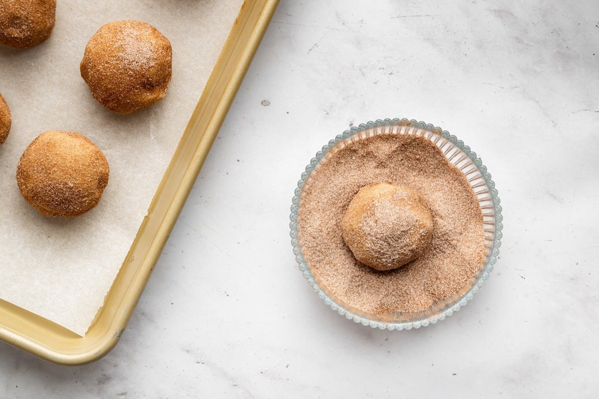 Snickerdoodle cookie dough ball being coated in cinnamon sugar.