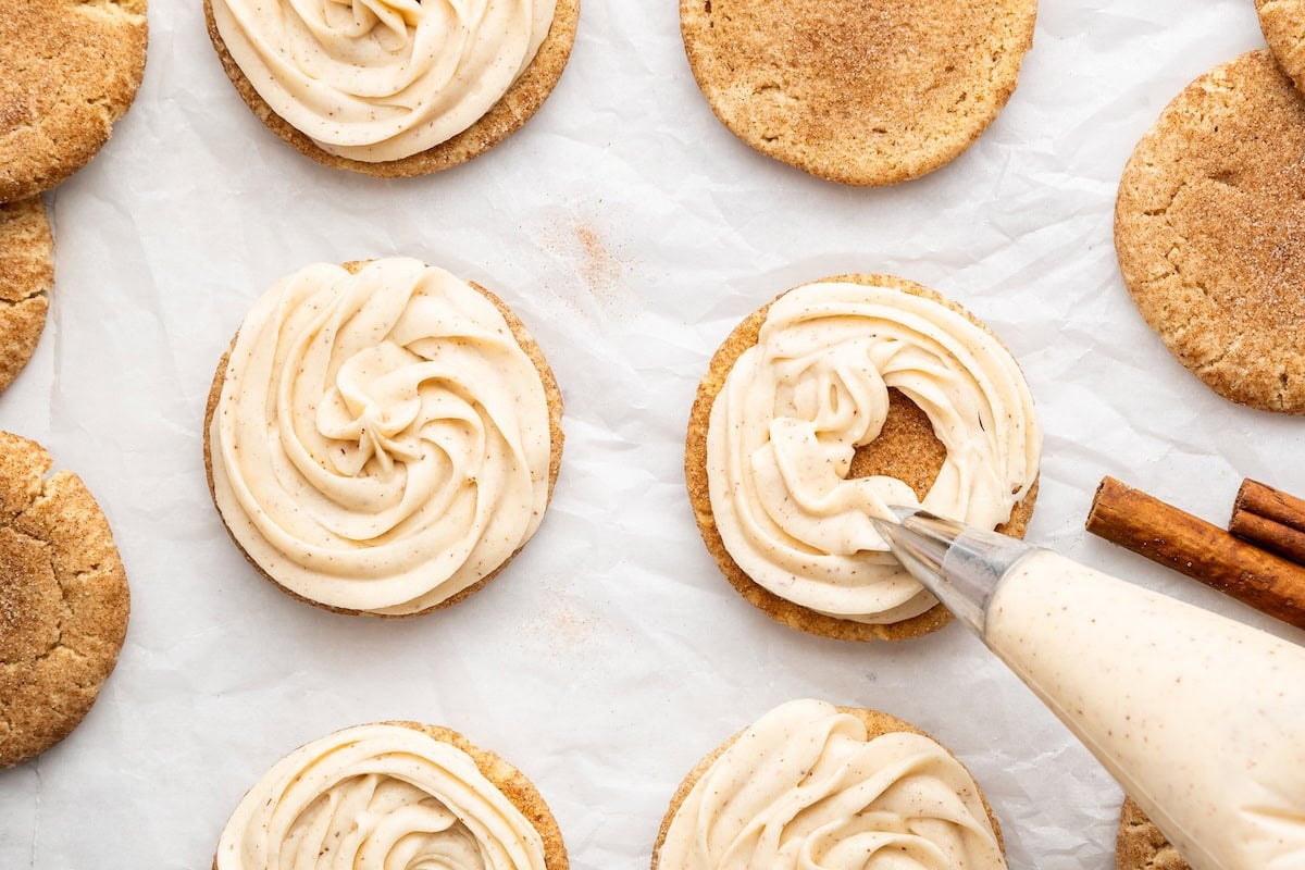 Cinnamon cream cheese frosting piped onto snickerdoodle cookies before assembling the sandwiches.