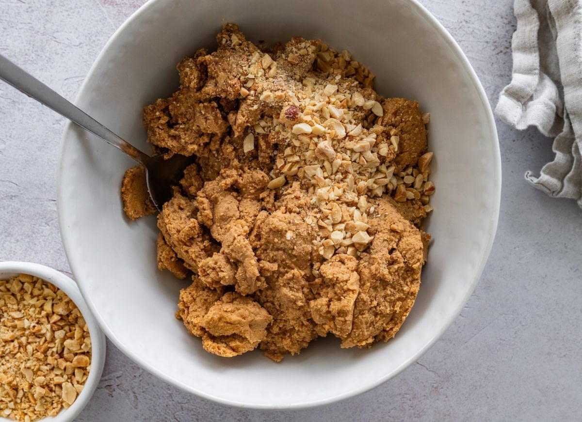 Snickers protein ball dough mixed with chopped peanuts in a bowl.