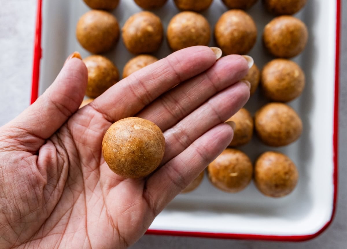 Hand holding a rolled Snickers protein ball with more uncoated balls on a baking sheet behind it.
