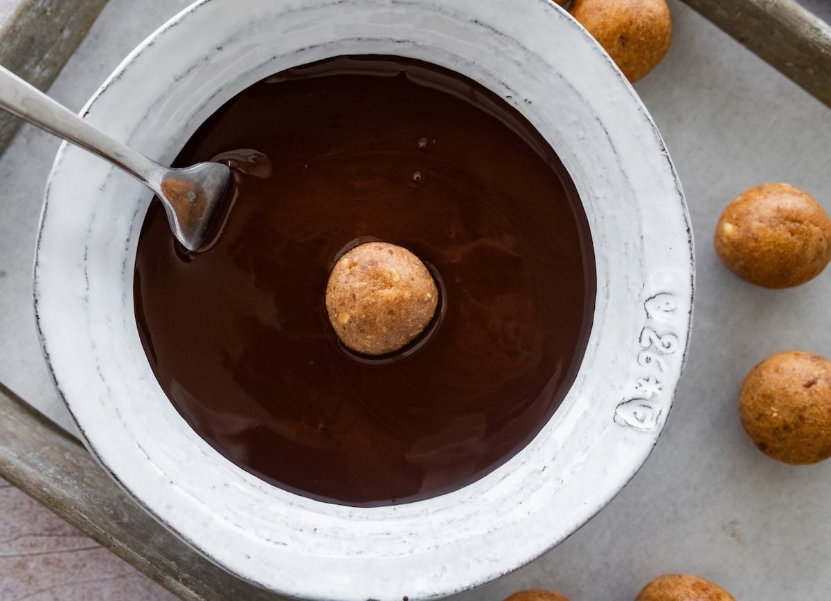 Peanut butter protein ball being dipped into melted dark chocolate.