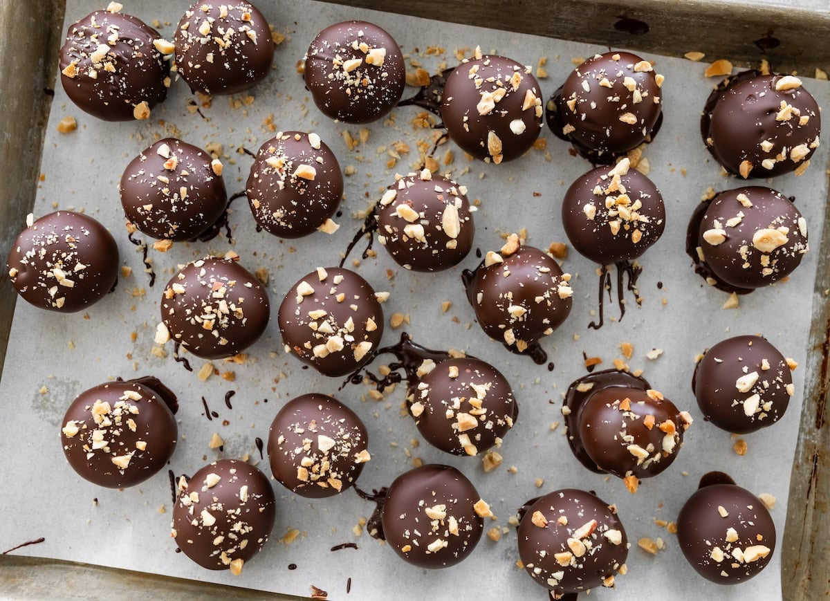 Chocolate-coated Snickers protein balls sprinkled with chopped peanuts on a parchment-lined baking sheet.