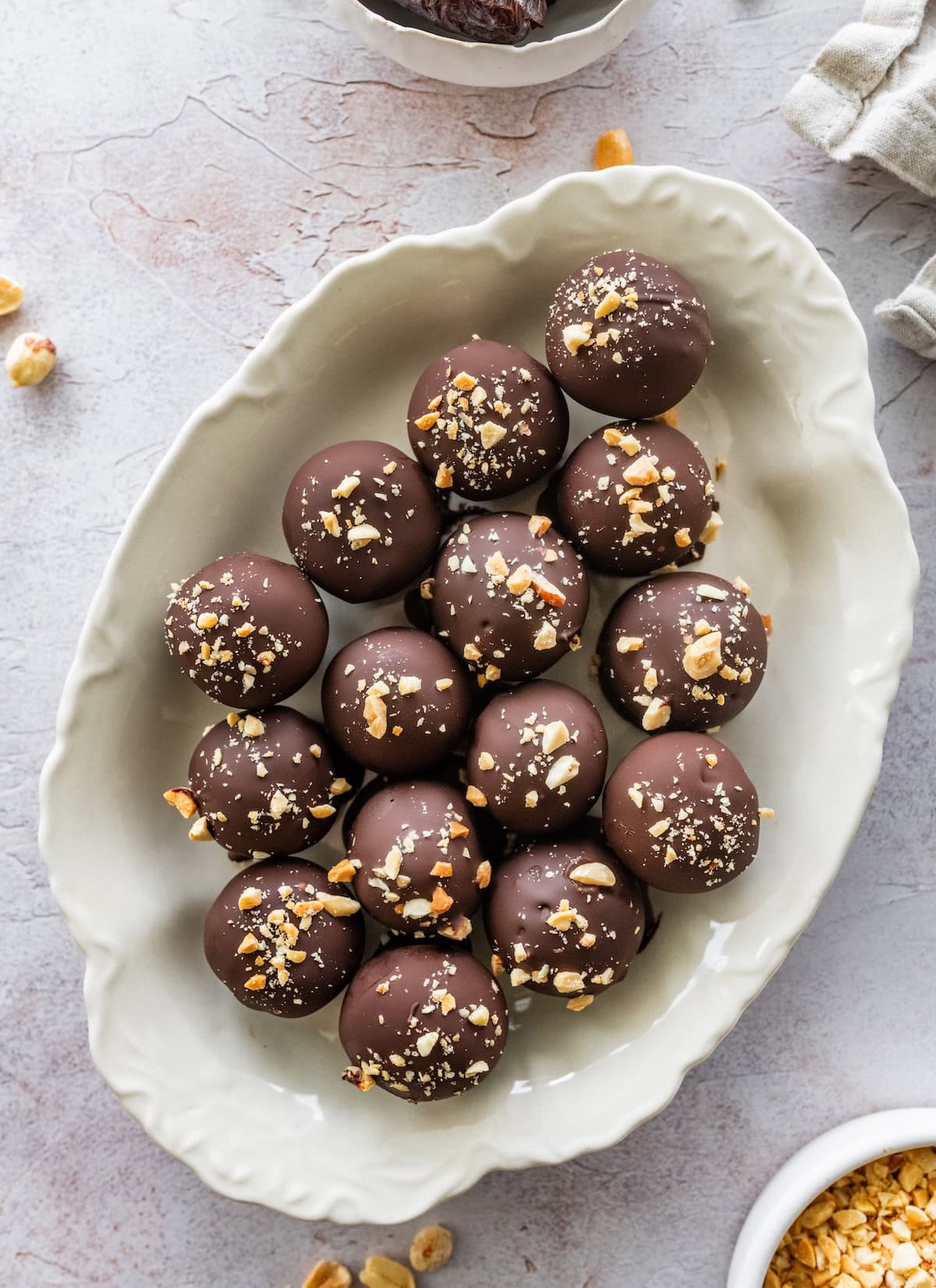 Chocolate-coated Snickers protein balls topped with chopped peanuts on a white serving platter.