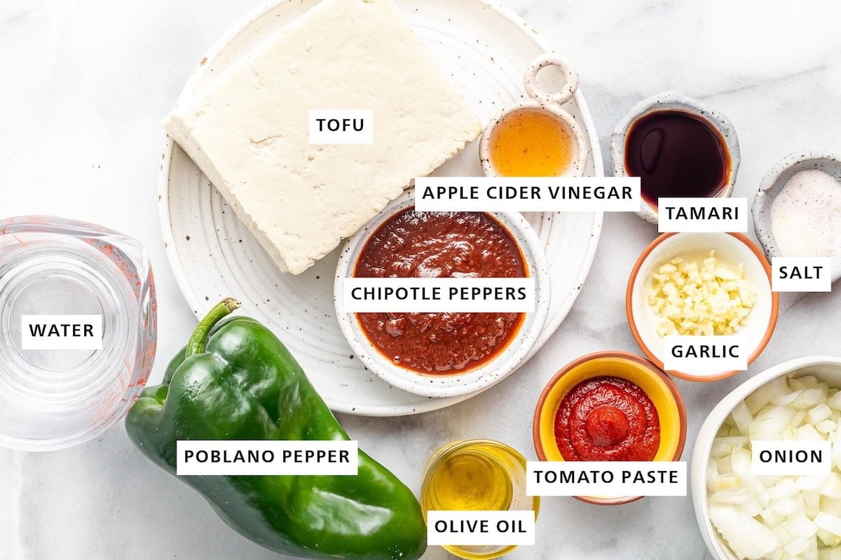 Ingredients measured out to make sofritas: water, poblano pepper, adobo chipotle pepper, tofu, vinegar, oil, tomato paste, garlic, soy sauce, salt and onion.
